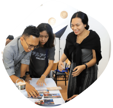 Three young Cambodians collaborate on an activity around a table while laughing.